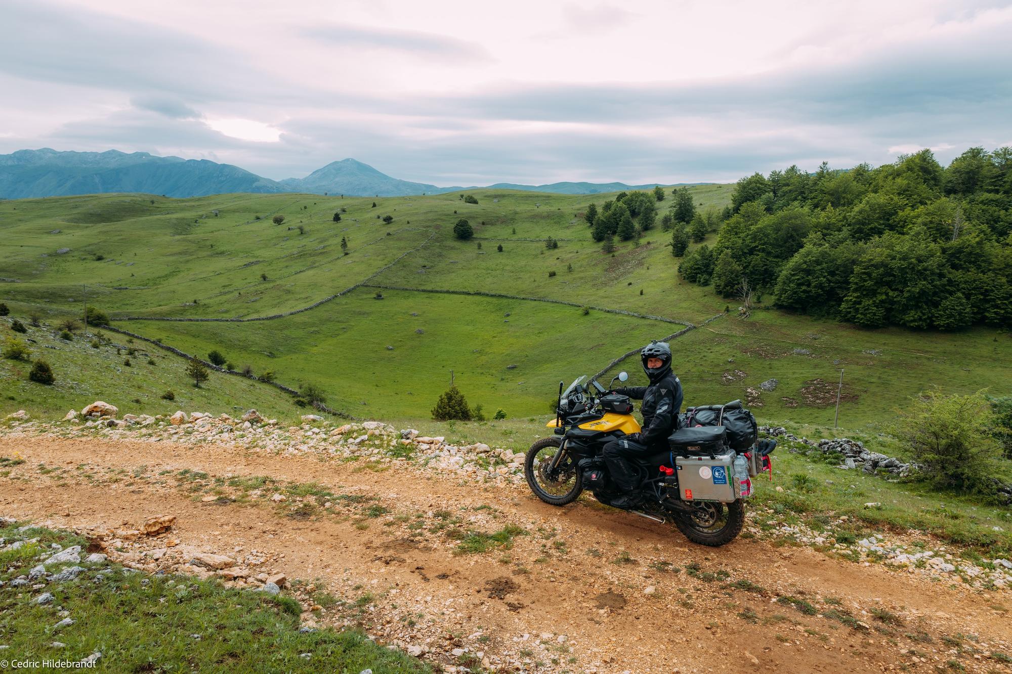 Cedric riding his motorcycle on a gravel track through the mountains of Bosnia