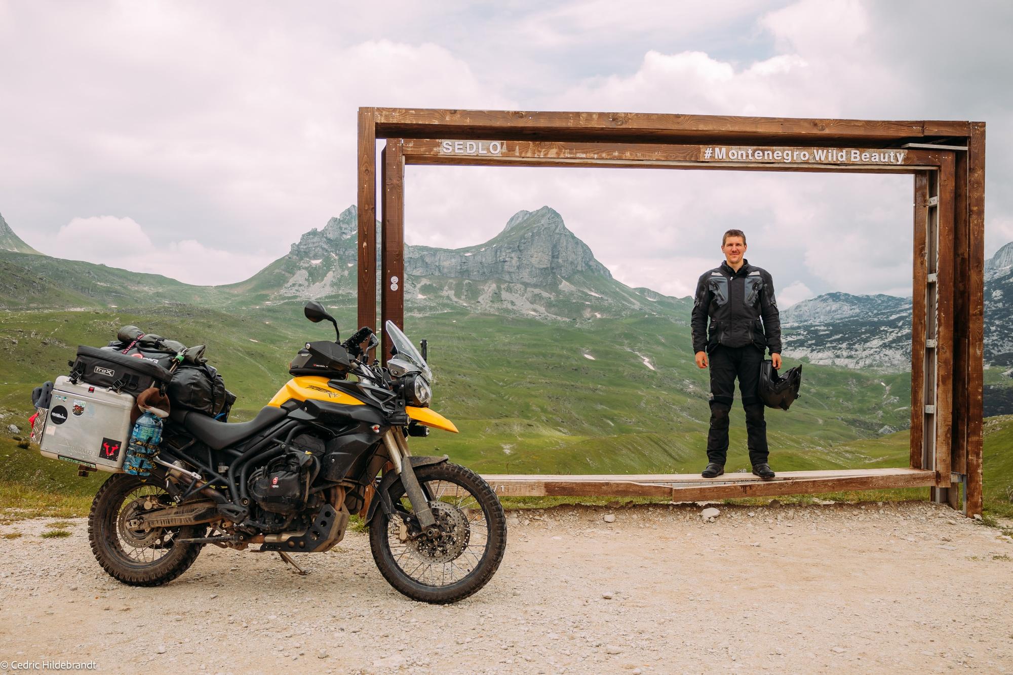 Cedric with his Triumph in front of a wooden frame in the mountains of Montenegro