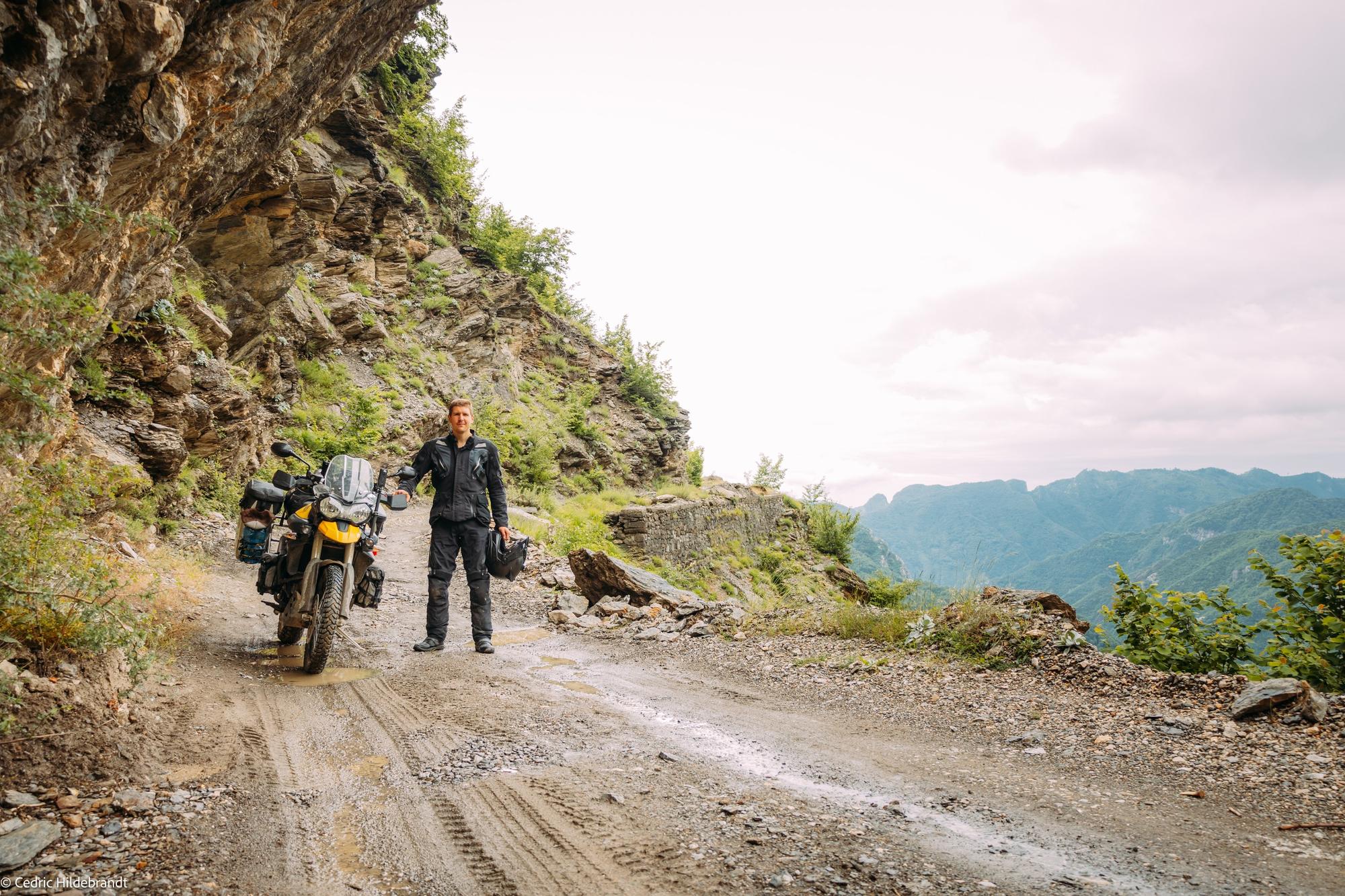 Cedric with his loaded motorcycle on a gravel road in Albania