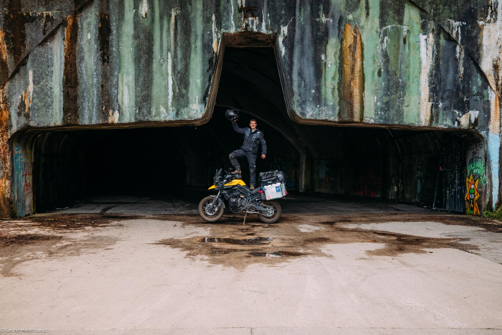Cedric with his motorcycle in front of an abandoned aircraft hangar in the Balkans