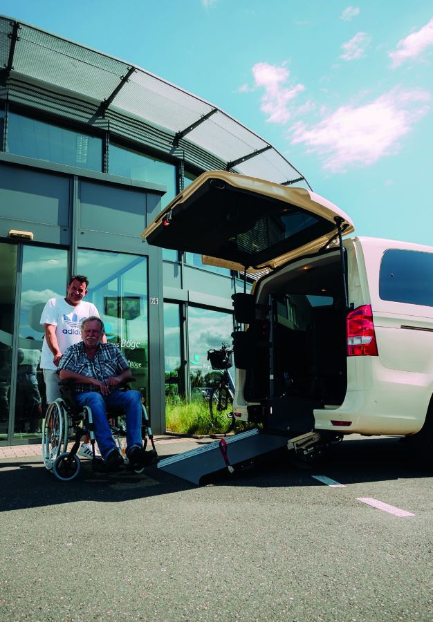 Driver pushes a passenger in a wheelchair to the wheelchair-accessible taxi